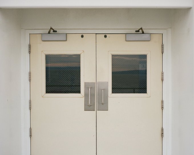 A pair of cream-colored double doors with wire-mesh glass windows, mounted on a plain white wall.