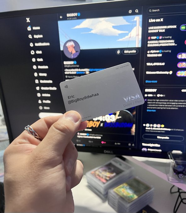 A hand holds up a silver Visa Debit/Flex card personalized with the name 'Eric @BigBoydidwhaa' in front of a computer monitor displaying the BigBoy Twitter/X profile.