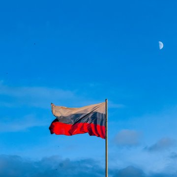 The Russian flag flies against a blue sky with the moon visible, symbolizing Russia's pioneering step as its Finance Ministry begins paying employee wages in digital rubles starting October 1.