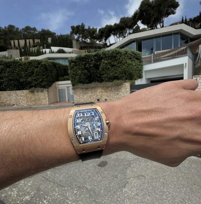 The image features a person wearing a gold watch with black numbers, which is positioned on their wrist. They are standing outside of a house or building, possibly admiring the architecture. The photo also includes text that reads "1 $SOL Just hit the like and say gm". This suggests that someone has taken this picture to share it on social media platforms, where they might want to highlight the watch's design or their appreciation for the location.

The person wearing the watch is positioned in front of a house with a garage door visible behind them. The image captures an interesting moment between the watch and its surroundings, creating a visually appealing composition that showcases both the timepiece and the building it is situated near.