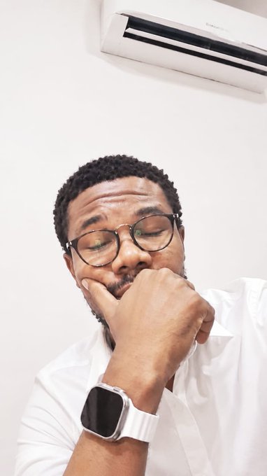 A man with glasses and a white shirt rests his hand thoughtfully against his chin beneath an air conditioner, appearing reflective. The contemplative pose mirrors the post's thoughtful tone about stepping away from social media to reflect on the shared mission of advancing the $WKC community's goals.