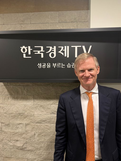 A man in a navy suit and orange tie smiles while standing in front of a sign reading "한국경제TV" (Korea Economic TV), suggesting the BitGo CEO Mike Belshe is in South Korea for an upcoming interview with the outlet.