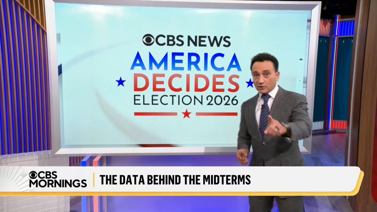 A male news anchor in a gray suit stands in a studio in front of a large screen displaying 'CBS NEWS AMERICA DECIDES ELECTION 2026', with a lower-third graphic reading 'CBS MORNINGS THE DATA BEHIND THE MIDTERMS'.