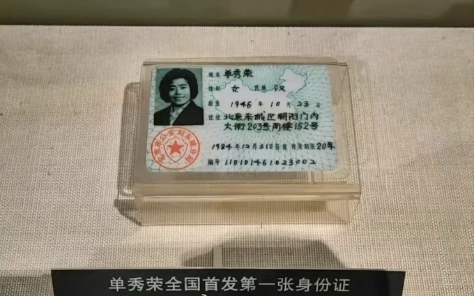 A museum display showing China's first ID card issued to Shan Xiurong (单秀荣) in 1984, with a placard reading '单秀荣全国首发第一张身份证' (Shan Xiurong's nationally first-issued ID card).