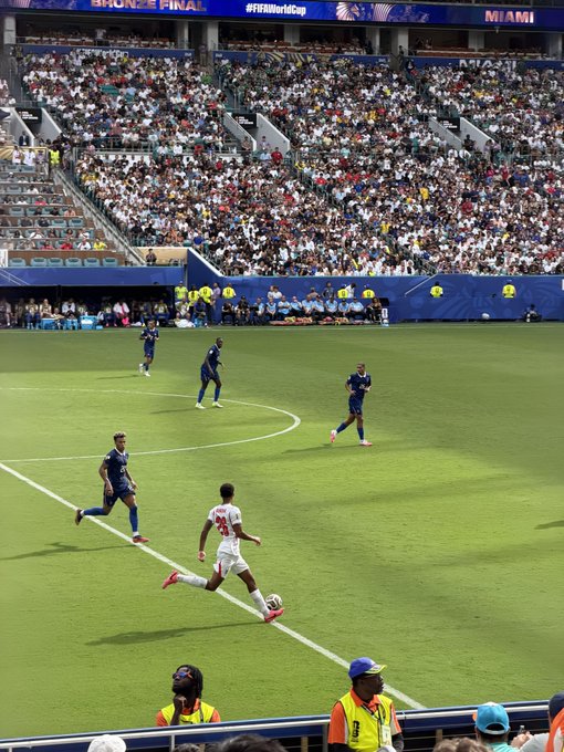 A soccer player in a white jersey dribbles the ball down the sideline during a match at what appears to be the 2019 FIFA Women's World Cup Bronze Final in Miami, as indicated by the "#FIFAWWC" banner visible in the stadium. The scene captures the moment of the French team referenced in the caption, with players in blue jerseys defending the play before a packed stadium crowd.