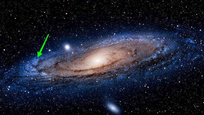 The image shows the Andromeda Galaxy with a green arrow pointing to a small blue dot, indicating Earth's location within the vastness of space. The caption "You are here, wondering if Bitcoin has bottomed" humorously contrasts the immense scale of the universe with the comparatively small concern of cryptocurrency market fluctuations, suggesting that even amid cosmic insignificance, investors fixate on short-term market movements.