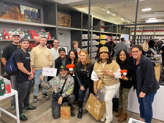 A group of people pose together inside what appears to be a retail store, with shelves of merchandise visible in the background.