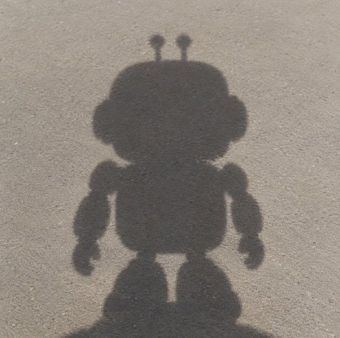 A robot-like shadow cast on a textured gray surface, featuring antennae and rounded limbs.