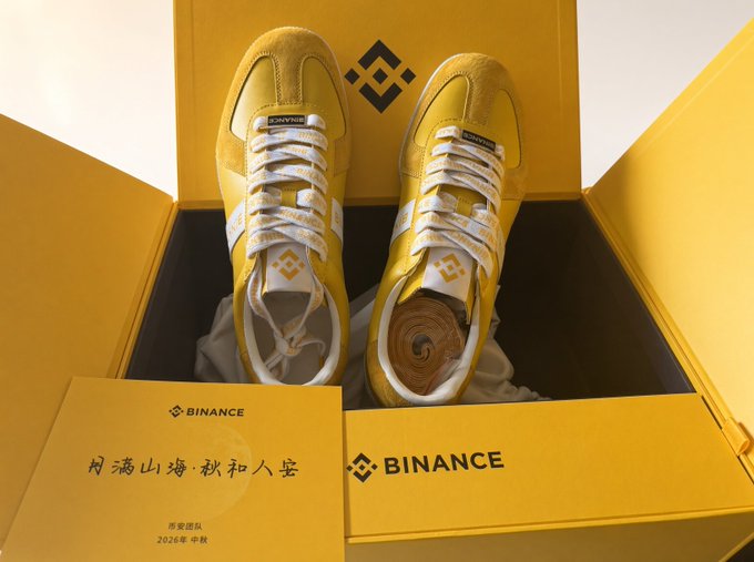 A pair of yellow and white Binance branded sneakers displayed in a yellow box with a Binance-branded envelope that reads 'Binance', '相濡以沫·秋和人宴', '币安团队', '2026年 中秋'.