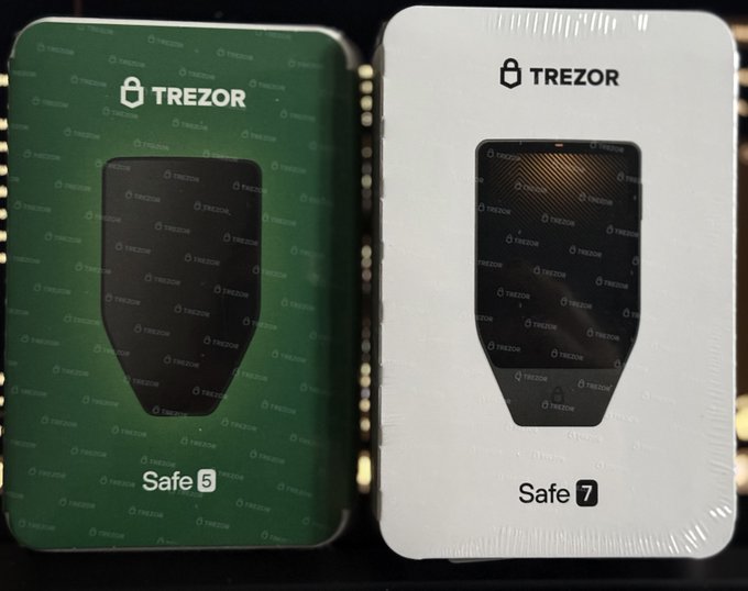 Two Trezor hardware wallet packages side by side: the green 'Safe 5' and the white/silver 'Safe 7' boxes, both factory-sealed.