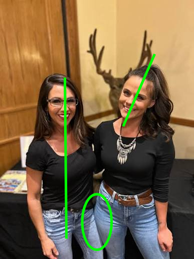 The image shows two smiling women posing together at what appears to be a conference or event, with antlers mounted on the wall behind them; green lines and a circle have been drawn on the image to highlight one woman's body curving inward while the other's curves outward, playfully illustrating the lyrics about the conflict between the mind saying no but the body saying yes.