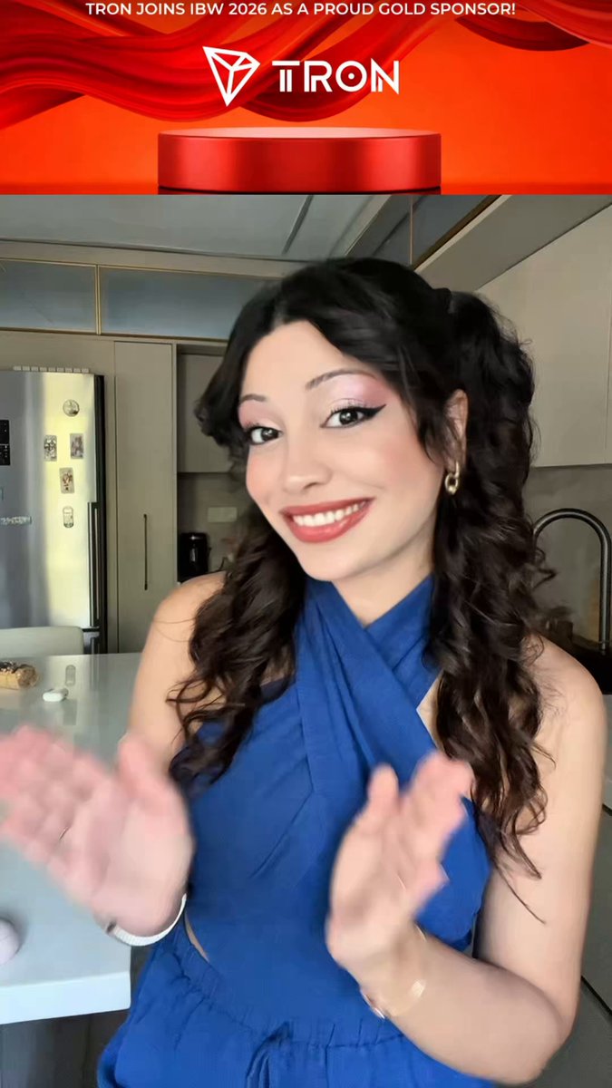 The image features a woman wearing a blue dress with her hands clapping together. She appears to be smiling, possibly posing for a photo or participating in an event. The background of the image shows a kitchen area with a refrigerator visible behind the woman. There is also text on the image that reads "TRON joins as proud sponsor Istanbul Blockchain Week 2026 was packed full this year too! The main sponsor TRON'S booth drew intense interest throughout the event, while new connections and Web3 chats never stopped."