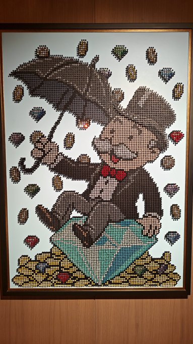 A framed pixel art or cross-stitch artwork depicting a character in a suit and red bow tie flying with an umbrella while holding a blue suitcase, surrounded by falling leaves and gold coins.