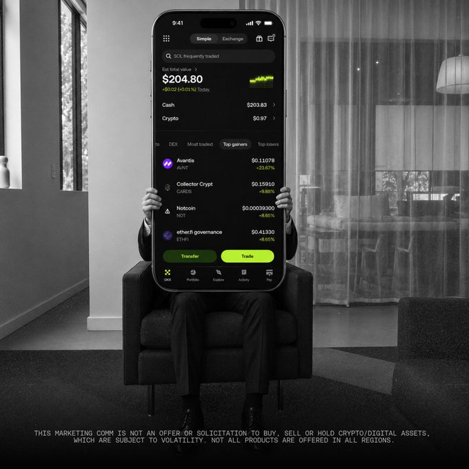Black and white image of a person sitting in a chair holding a large smartphone displaying the Simple Exchange app, showing a portfolio value of $204.80 with holdings in Avantis, Collector Crypt, Notcoin, and ether.fi governance.