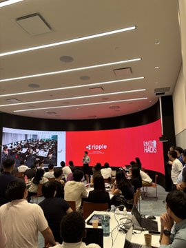 A crowded conference or talk event with 'ripple' and 'HOPE' branding on a red screen, with a speaker on stage and audience members seated at tables.