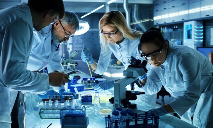 A diverse team of scientists in white lab coats works intently at a bench filled with pipettes, test tubes, and microscopes in a high-tech research laboratory, embodying the collaborative pursuit of future scientific breakthroughs.

The image ties to "WHAT'S NEXT?" by capturing the hands-on research and innovation driving tomorrow's discoveries.