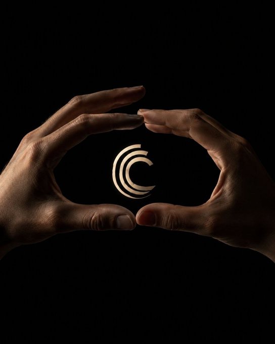 Two hands form a circular frame against a black background, enclosing a glowing gold geometric 'C' logo in the center.