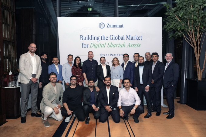 A diverse group of business professionals poses in front of a banner reading "Zamanat - Building the Global Market for Digital Shariah Assets," representing the institutional partnerships and real capital infrastructure mentioned in the post about ZIGChain's RWA launch and $ZIG buybacks.