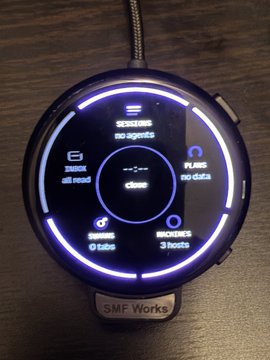 A circular smartwatch labeled 'SMF Works' displaying a neon-bordered interface with options for 'Status', 'Assets', 'Combo', 'Blinks', 'Chains', 'Anomaly', and 'Tabs', currently showing 'close'.