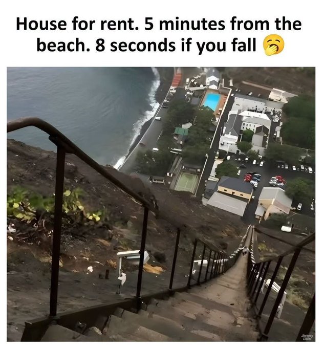 A meme showing a steep staircase descending from a cliff to a coastal town below, with text reading 'House for rent. 5 minutes from the beach. 8 seconds if you fall 😏'