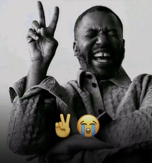 A black and white image of a laughing man making a peace sign, with a yellow peace sign emoji and a crying-laughing emoji overlaid at the bottom.