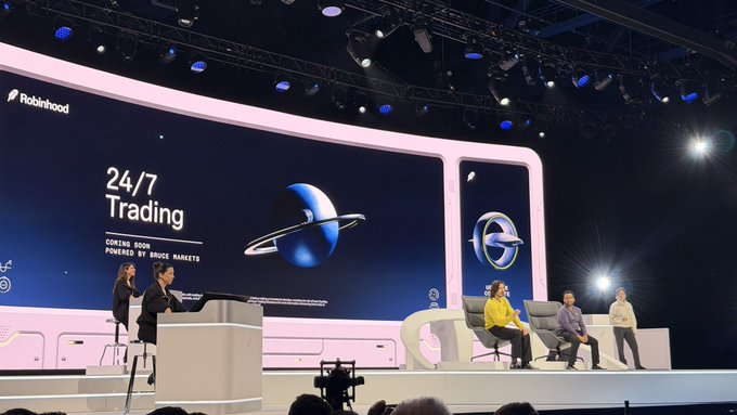 A stage presentation at a Robinhood event discussing '24/7 Trading' powered by Bruce Markets, with speakers seated on stage alongside a planet-themed visual.