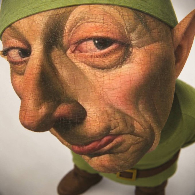 The image shows a close-up of a weathered, antique-looking doll or figurine with an aged, cracked painted face, pointed ears, and a green felt cap and outfit, possibly resembling a goblin or elf character.