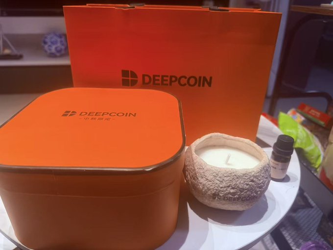 An orange tin and matching shopping bag both labeled 'DEEPCOIN' are displayed next to a coconut-shaped candle on a white plate.