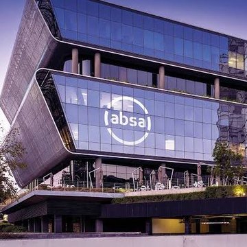 An evening photograph of the modern, angular glass facade of the Absa building, featuring the '(absa)' logo illuminated on its reflective surface.
