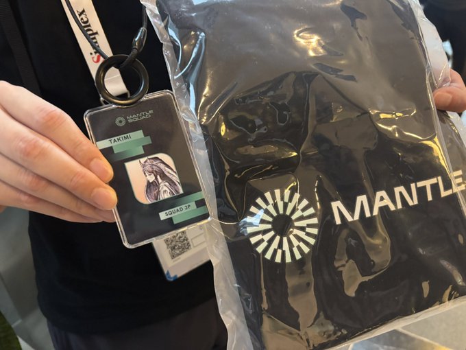 A person holding a lanyard with a "MANTLE SQUAD" badge and a sealed black "MANTLE" merchandise bag.