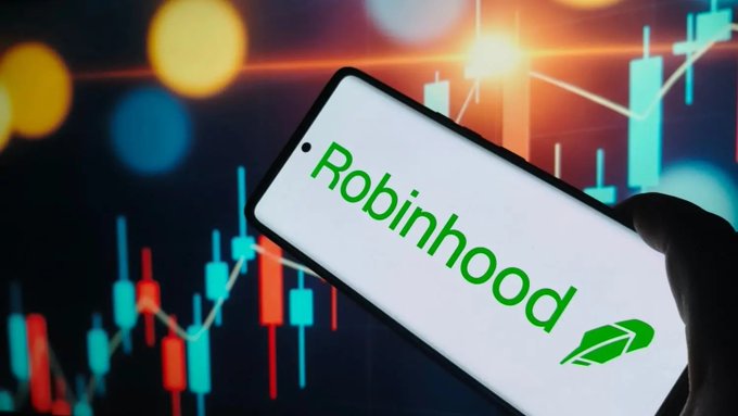 A hand holds a smartphone displaying the green 'Robinhood' logo and feather icon, set against a background of colorful stock market candlestick charts.