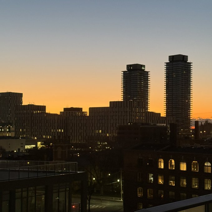 A city skyline at sunset with two tall residential towers silhouetted against an orange and blue horizon, while building lights begin to glow below, evoking the calm close of a day. The image ties to the caption's "Good night CT" greeting, visually framing the post's message about Tria's simplified crypto experience as a peaceful end-of-day reflection on practical, self-custodial finance.