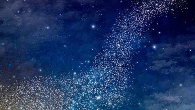 A nighttime photograph of a starry sky featuring the Milky Way, with countless bright stars scattered across deep blue clouds and nebulae.