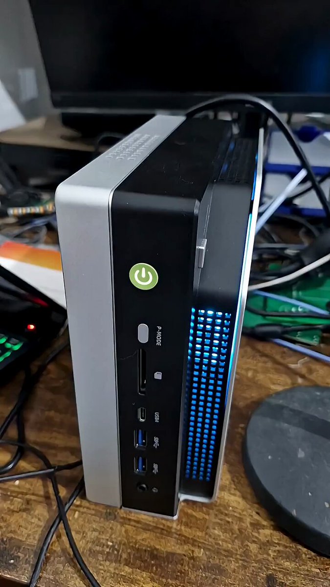 The image shows a desktop computer tower with various ports, including multiple USB cables and a power cord running from the back of the computer, all connected to an external monitor that is located near several other miscellaneous items such as a printer, a keyboard, and potentially some other electronic devices. The computer appears to be turned on but has not been used yet. There's also a green button on the side of the computer tower, which may be related to controlling certain functions or settings within the system.