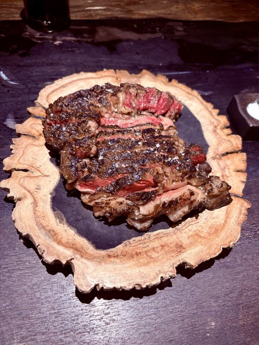 A perfectly seared, sliced ribeye steak rests on a rustic live-edge wooden board, its pink, juicy interior contrasting with the charred, peppered crust. This mouthwatering presentation serves as visual confirmation—the "proof"—that the steak is cooked to a flawless medium-rare.