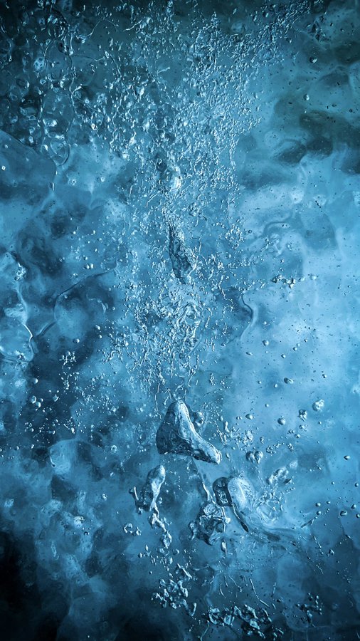 A vertical image looking up through clear blue water, filled with rising bubbles and light refractions.