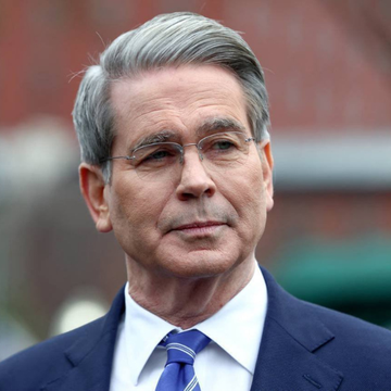 A portrait photo of an older man with gray hair, glasses, a mustache, wearing a dark blue suit and blue striped tie.