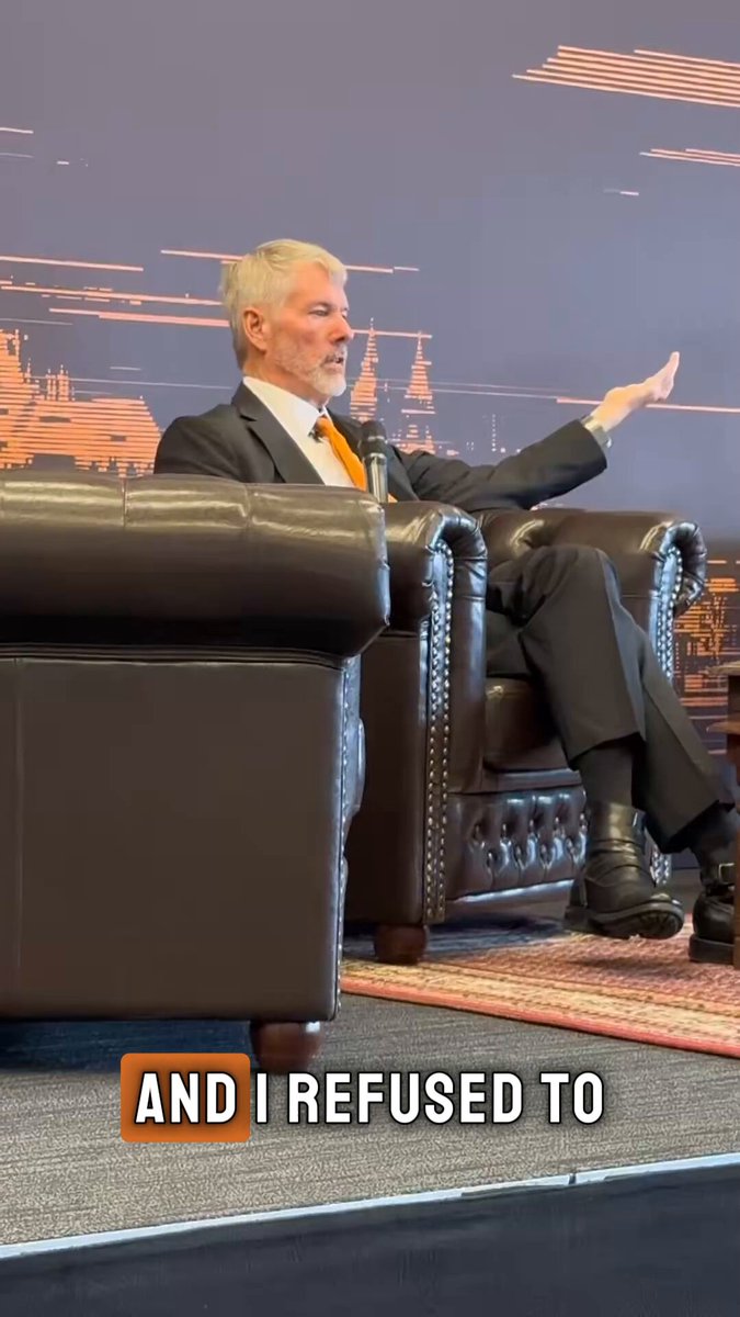 The image features an older man sitting in a chair with his arms outstretched as if he's giving a speech or making a gesture. The background of the image shows a wall, which could be part of a presentation room for a business event. There is also text on the image that reads "And I refused to sell my Bitcoin". This suggests that the man might have been discussing Bitcoin and its value during his speech at the event.