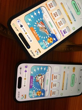The image shows two cell phones placed side by side, both displaying a game screen with colorful graphics and icons. The phones are positioned at different angles, creating an interesting visual effect. The background of the image features a wooden surface, which complements the overall aesthetic of the scene.