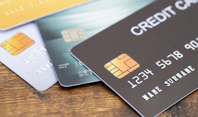 A close-up photograph of four overlapping credit cards in yellow, white, green, and black resting on a wooden surface.