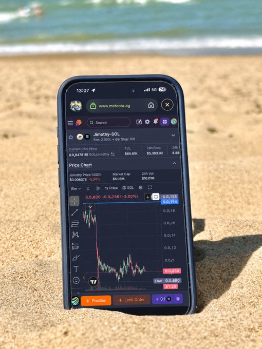 A smartphone on a sandy beach displays a trading chart for Jimothy-SOL on meteora.ag, showing a current price of approximately 0.0479 US.