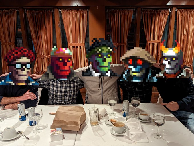 A group of five people sit together at a restaurant table with coffee cups and drinks, with pixelated character avatars replacing their faces.