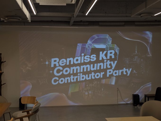 A photo of a dimly lit room with a large projection screen displaying 'Renaiss KR Community Contributor Party' with a holographic gift box graphic.