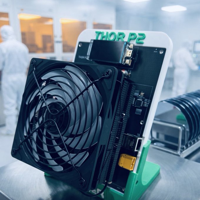 Image of a mining device or ASIC labeled 'THOR P2' with a large cooling fan, displayed in a clean room environment with workers in white suits.