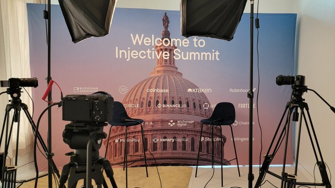 A professional broadcast setup with cameras, lighting, and chairs arranged in front of a "Welcome to Injective Summit" backdrop featuring the U.S. Capitol and sponsor logos (Coinbase, Kraken, Robinhood, Circle, BinanceUS, Chainalysis, Coinbase, Canary Capital, Steak 'n Shake, and Coinbase), ready for the Blockchain Association's policy summit tomorrow.