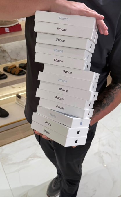 A person holding a tall stack of white Apple iPhone boxes in what appears to be a retail store setting.