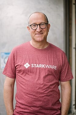A man wearing glasses and a red "STARKWARE" t-shirt poses for a portrait. The image appears to relate to the post as Eli Ben-Sasson is the founder of StarkWare, a company he started after his foundational work on Zcash ($ZEC), connecting his current enterprise to his earlier crypto privacy work.