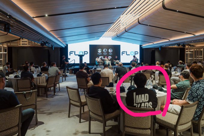 A panel discussion event with 'FLOP' displayed on screens, where an audience member wearing a shirt that reads 'I MAD FANS' is highlighted with a pink circle.