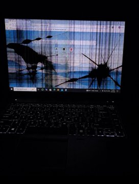 A close-up of a laptop screen in a dark room displaying a cracked or shattered visual effect with bluish horizontal lines.