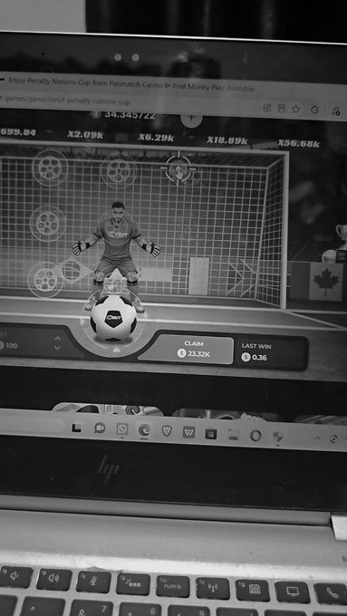 A black-and-white photo shows a laptop screen displaying a "Penalty Nations Cup" soccer penalty shootout game on Parimatch casino, featuring a goalkeeper standing in front of the net with various multipliers (X2.09k, X6.29k, X16.89k, X56.66k) visible at the top. The claim of $23.32K on screen reflects the user's boast of turning $100 into $23k, with the last win showing $0.36 still pending, aligning with the post's message of cashing out.